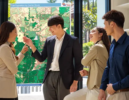 Four colleagues talking beside a wall map of total population by carrier route, its routes shaded in greens and yellows.