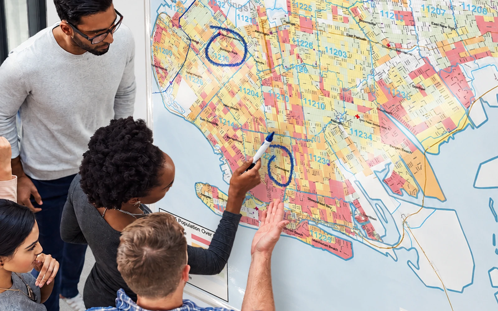 Four colleagues around a large laminated map, one drawing on it with a marker