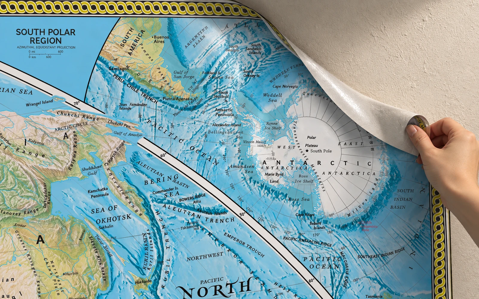 A hand peeling the corner of a map mural away from the wall