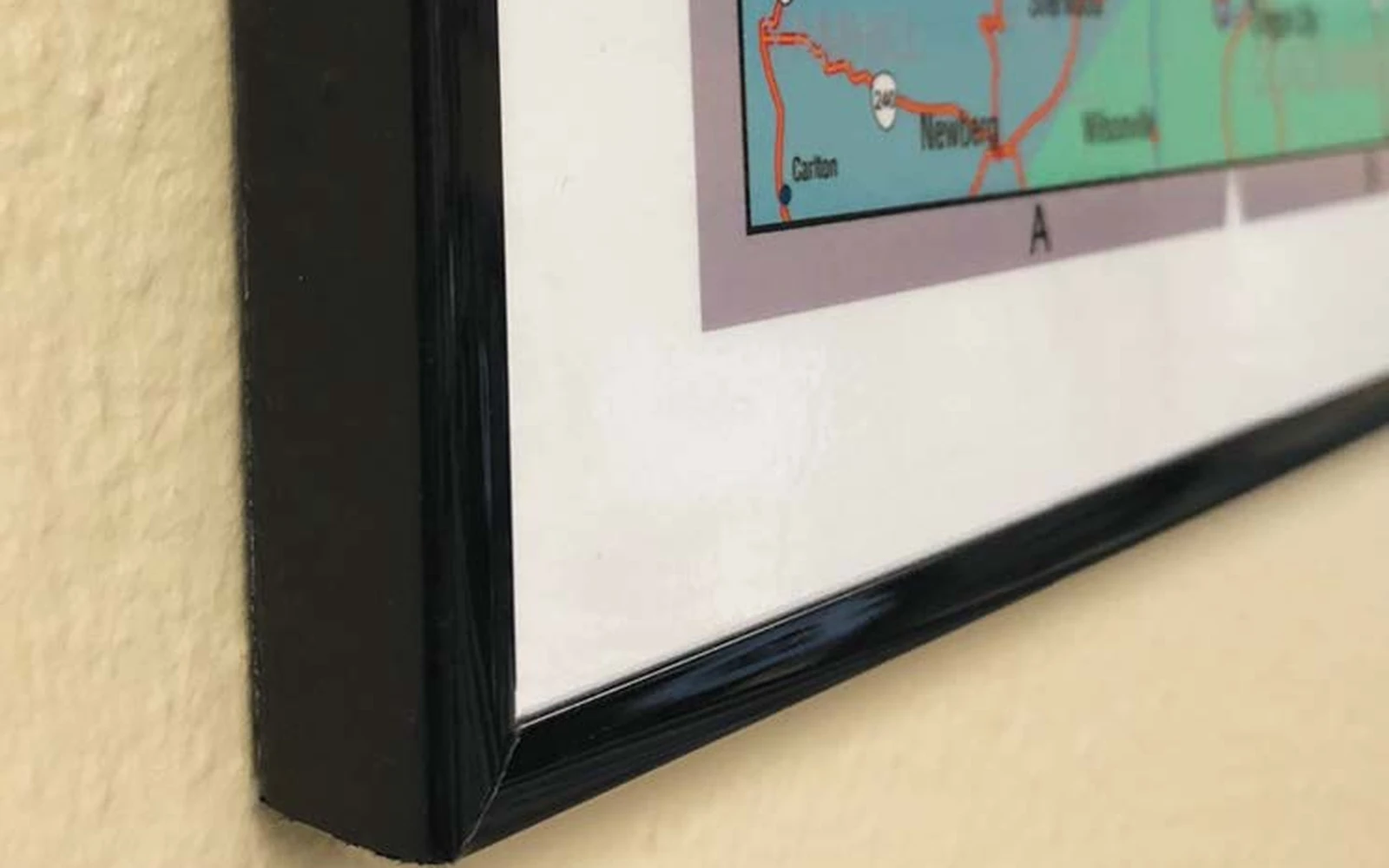 The lower corner of a black plastic framed map against a wall