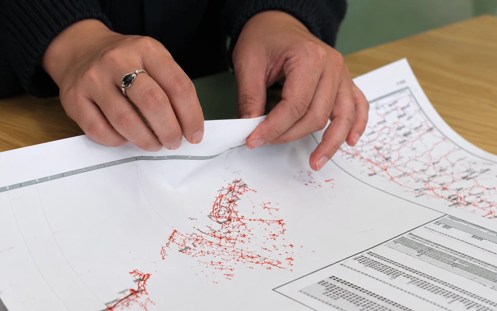 Hands folding a synthetic paper map flat against a desk